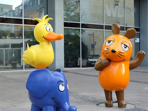 Sendung mit der Maus Ensemble vor dem WDR Köln Maus, Elefant und Ente als bunte Figuren vor der Glasfassade des WDR in Köln