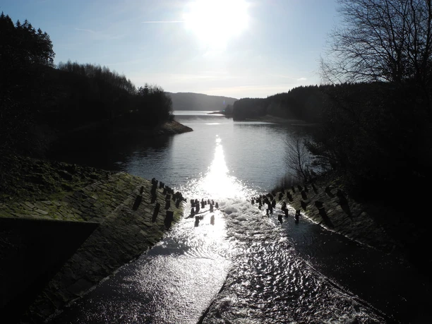 Eindrücke am Wegesrand Blick auf einen bei Sonnenuntergang glitzernden Fluss, umgeben von bewaldeten Ufern und Hügeln.