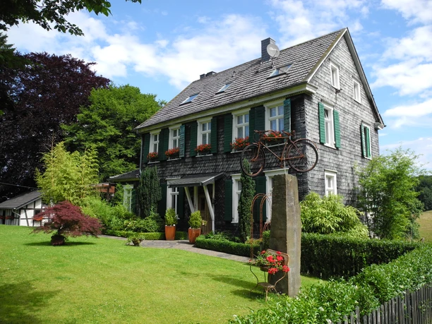 Eindrücke am Wegesrand Ein zweigeschossiges Fachwerkhaus mit Schieferfassade, grünen Fensterläden und gepflegtem Garten.