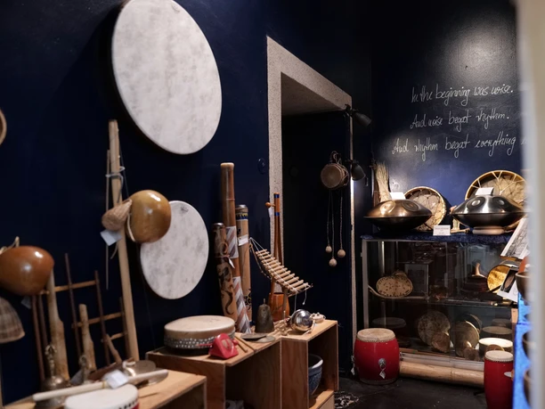 Die Wand ist dunkelblau, davor stehen Regale mit Musikinstrumenten.