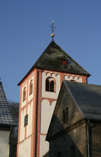 Sankt Pankratius in Odenthal Roter Kirchturm einer romanischen Kirche mit blauen Himmel und Teilen eines angrenzenden Gebäudes.