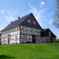Schultheißmühle Ein traditionelles Fachwerkhaus mit schwarzem Holz und weißen Wänden auf grünem Hügel bei blauem Himmel.