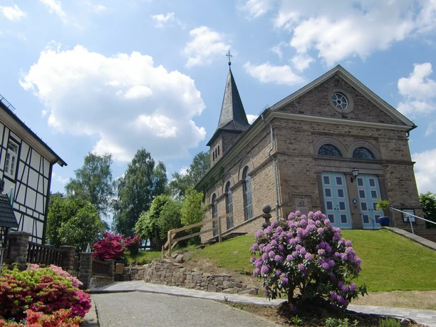 Ev. Kirche Delling <p>Eine malerische Kirche in Kürten, umgeben von blühenden Rhododendren unter blauem Himmel.</p>