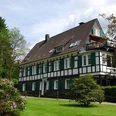 Berger Mühle Historisches Fachwerkhaus mit weißen Wänden, grünen Fensterläden, umgeben von Garten und Bäumen.