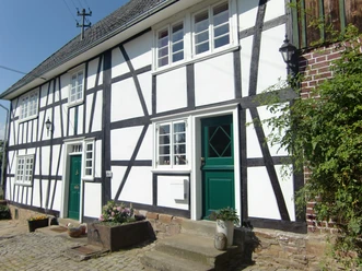 Fachwerkdorf Benroth Fachwerkhaus mit weißen Wänden und schwarzen Balken, grüne Türen und Pflanzkübel auf Kopfsteinpflaster.