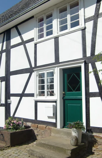 Fachwerkdorf Benroth Fachwerkhaus mit weißen Wänden und schwarzen Balken, grüne Türen und Pflanzkübel auf Kopfsteinpflaster.