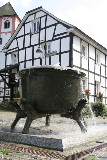 Hexenbrunnen Ein großer, antiker Bronze-Kesselbrunnen in einem gepflasterten Hof vor einem Fachwerkhaus.