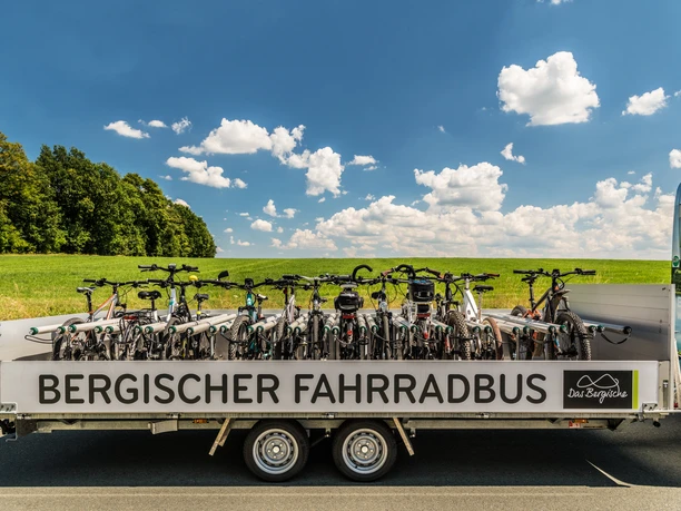 Bus mit Fahrradanhänger Fahrradanhänger voller Fahrräder vor ländlicher Kulisse unter blauem Himmel.