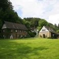 Steiner Mühle Fachwerkhäuser mit grünen Wiesen, umgeben von dichten Wäldern unter einem bewölkten Himmel.