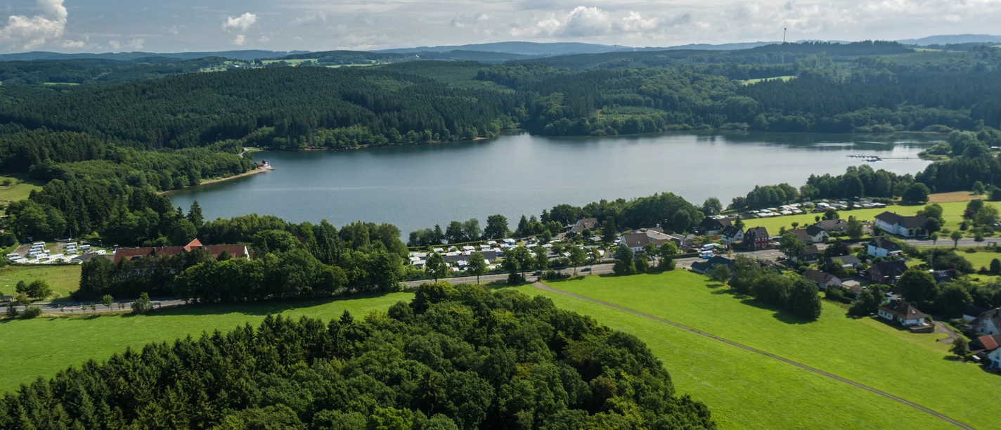 Brucher-Talsperre Marienheider Stausee, von Wald und Wiesen umgeben, bei sonnigem Wetter mit vereinzelten Wolken.