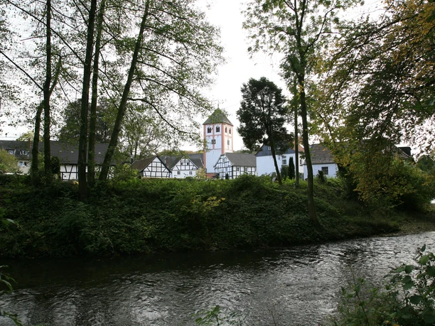 Die Dhünn in Odenthal Historisches Dorf mit Fachwerkhäusern und Kirchturm, eingebettet in üppige grüne Landschaft am Fluss.