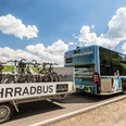 Bergischer FahrradBus Ein moderner Bus mit Fahrradanhänger auf einer Landstraße unter blauem Himmel mit Wolken.