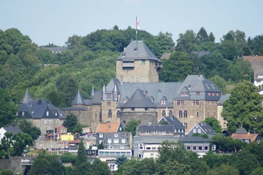 Schloss Burg in Solingen Blick auf eine mittelalterliche Burg mit hohen Türmen, umgeben von üppiger grüner Vegetation.