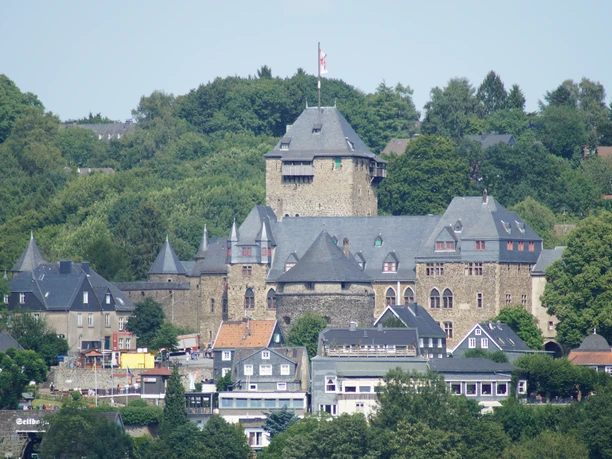 Schloss Burg in Solingen Blick auf eine mittelalterliche Burg mit hohen Türmen, umgeben von üppiger grüner Vegetation.