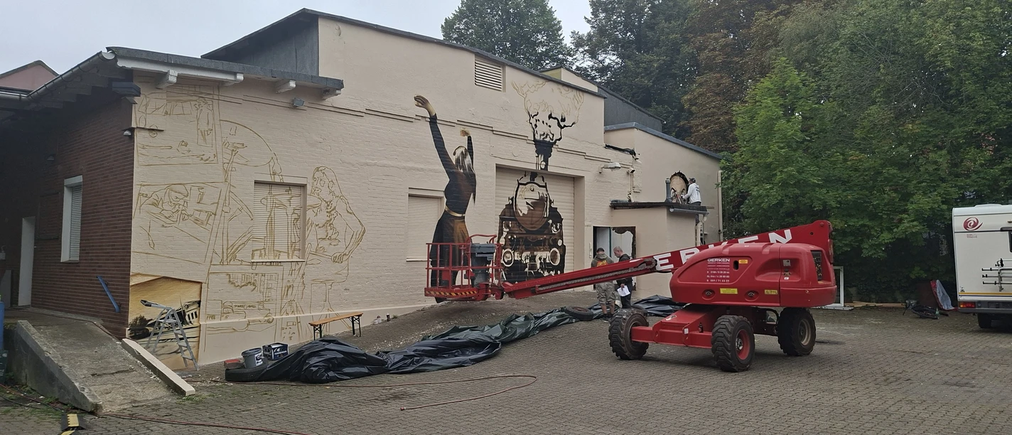 Yardparty Künstler gestalten ein Wandbild am Kulturbahnhof Lehe mit roter Hebebühne.