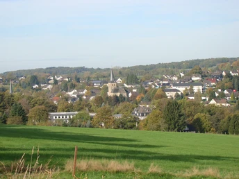 Ruppichteroth im Herbst, mit grünen Wiesen, zahlreichen Häusern und einer Kirche in der Ferne.