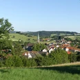 Blick über grüne Wiesen und Bäume auf das Dorf Sandebeck mit seiner markanten Kirchturmspitze im Zentrum.