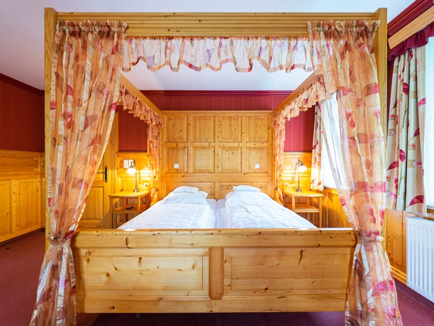 Doppelzimmer Hengstforder Mühle.jpeg Hotelzimmer im Landgasthof mit hölzernem Himmelbett und gemusterten Vorhängen.