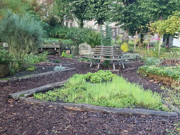 Bibelpflanzgarten Garten mit Sitzbank, bepflanzten Beeten und bunten Blumen, umgeben von Bäumen und Sträuchern.