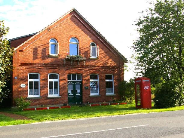 Hausfront.JPG Rotes Backsteinhaus mit grüner Tür und roter Telefonzelle am Straßenrand