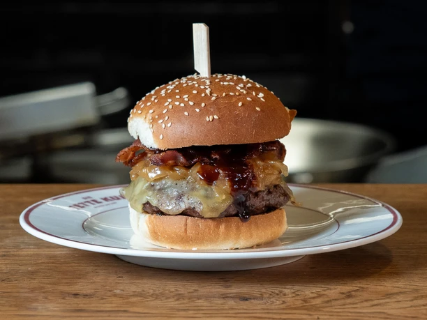 Die Fette Kuh - BBQ Bacon Cheeseburger BBQ Bacon Cheeseburger on a sesame bun, served on a plate at Die fette Kuh