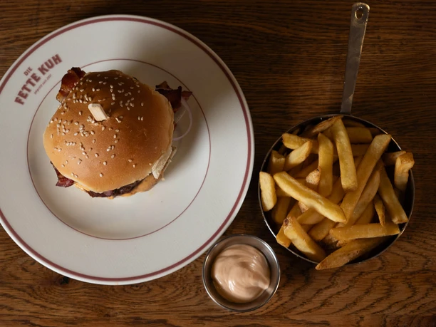 Die Fette Kuh - Burger und Pommes Burger auf Teller der Fetten Kuh mit Pommes und Dip auf Holztisch