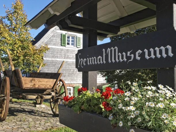 Heimatmuseum in Eckenhagen Historisches Gebäude mit Holzwagen und Blumenkasten im Vordergrund, Beschilderung "Heimatmuseum".