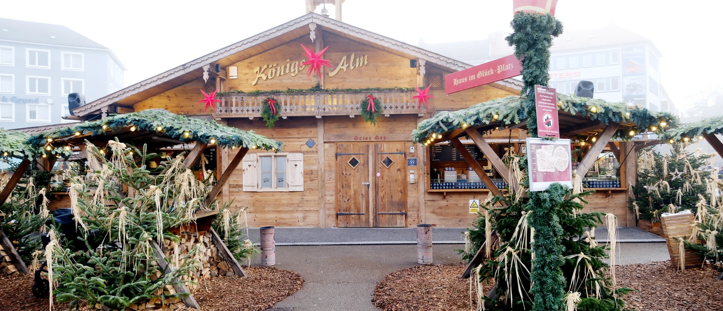 Die urige Hütte der Königsalm ist im Hintergrund sichtbar, davor sind weihnachtlich angerichtet überdachte Stehmöglichkeiten.