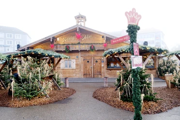 Königsalm | Märchenweihnachtsmarkt Kassel Die urige Hütte der Königsalm ist im Hintergrund sichtbar, davor sind weihnachtlich angerichtet überdachte Stehmöglichkeiten.