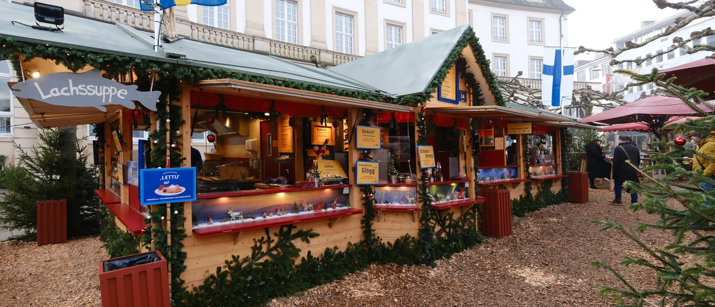 Finnenstand | Märchenweihnachtsmarkt Kassel Links hängt an der Holzhütte ein Schild mit "Lachssuppe". Die Hütte ist aus Holz und weihnachtlich geschmückt.