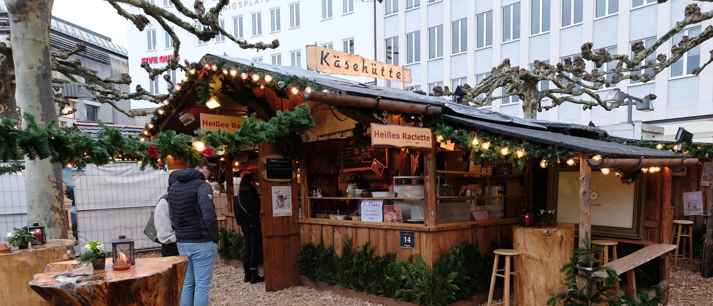 Käsehütte | Märchenweihnachtsmarkt Kassel Auf dem Boden vor der Käsehütte ist Mulch verteilt. Die Käsehütte ist aus Holz und weihnachtlich geschmückt.