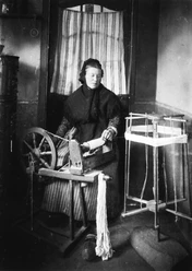 Leinenspinnen- traditionelle Heimarbeit Eine Frau spinnt Leinen an einem alten Spinnrad, umgeben von traditionellen Webutensilien.