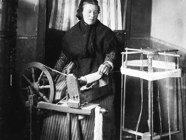 Leinenspinnen- traditionelle Heimarbeit Eine Frau spinnt Leinen an einem alten Spinnrad, umgeben von traditionellen Webutensilien.