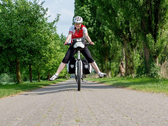 Radtour durch das Osnabrücker Land Radfahrer auf ländlichem Weg, breit lächelnd, Hände los, umgeben von grünen Bäumen und Natur.