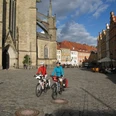 Marktplatz Osnabrück Zwei Radfahrer vor historischer Kirche und farbenfrohen Gebäuden in Osnabrück.