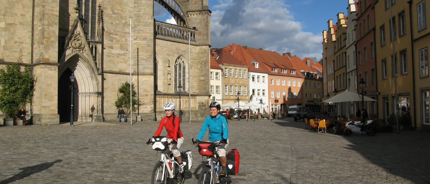 Marktplatz Osnabrück Zwei Radfahrer vor historischer Kirche und farbenfrohen Gebäuden in Osnabrück.