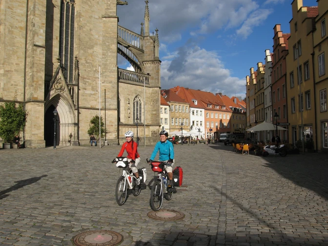 Marktplatz Osnabrück Zwei Radfahrer vor historischer Kirche und farbenfrohen Gebäuden in Osnabrück.