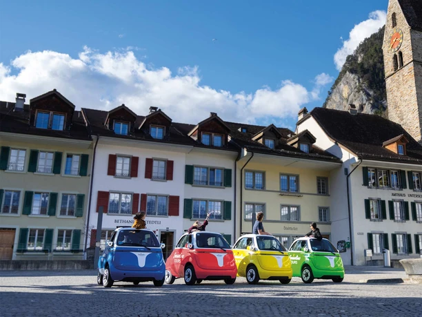 Four colorful Swissolino electric cars on Stadthausplatz in Unterseen, in front of the church