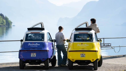 Deux petites voitures Swissolino au bord du lac de Brienz, avec des passagers, devant un décor montagneux
