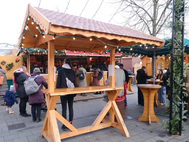 Heiße Quelle | Märchenweihnachtsmarkt Kassel Ein überdachter Holztisch mit Lichterkette. Im Hintergrund befindet sich der Getränkestand mit einigen Personen-