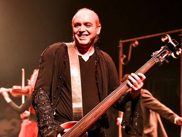 Cirque Bouffon Harmonia - Die Weihnachtsshow Lächelnder Bassist auf rot beleuchteter Bühne des Cirque Bouffon