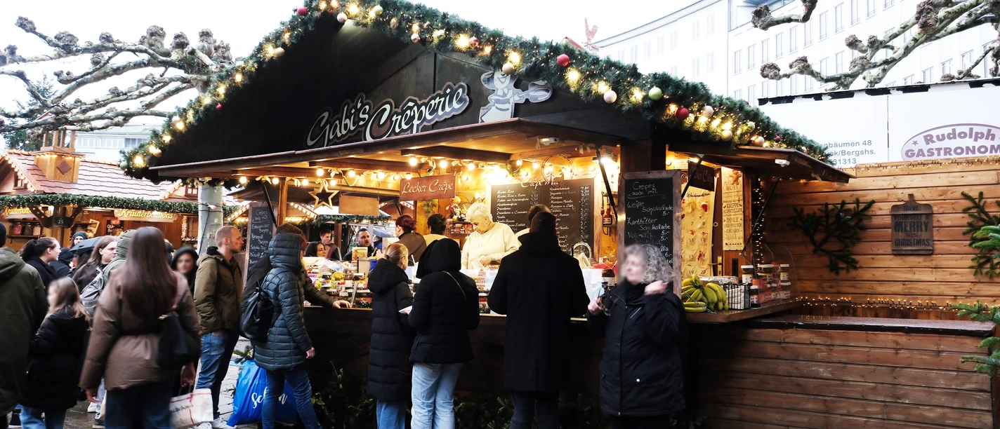 Gabis Creperie | Märchenweihnachtsmarkt Kassel Eine weihnachtlich verzierte Holzhütte mit mehreren Personen befindet sich im Bild.