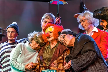 De letzte Kroog vör Helgoland oder De Bratfisch-Revue Theaterensemble in bunten Kostümen mit Clownsnase und Schirm auf der Bühne.