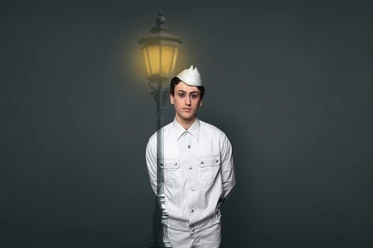 Die Leben der Andersen im Stadttheater Bremerhaven Schauspieler in weißer Uniform vor dunklem Hintergrund und leuchtender Laterne.