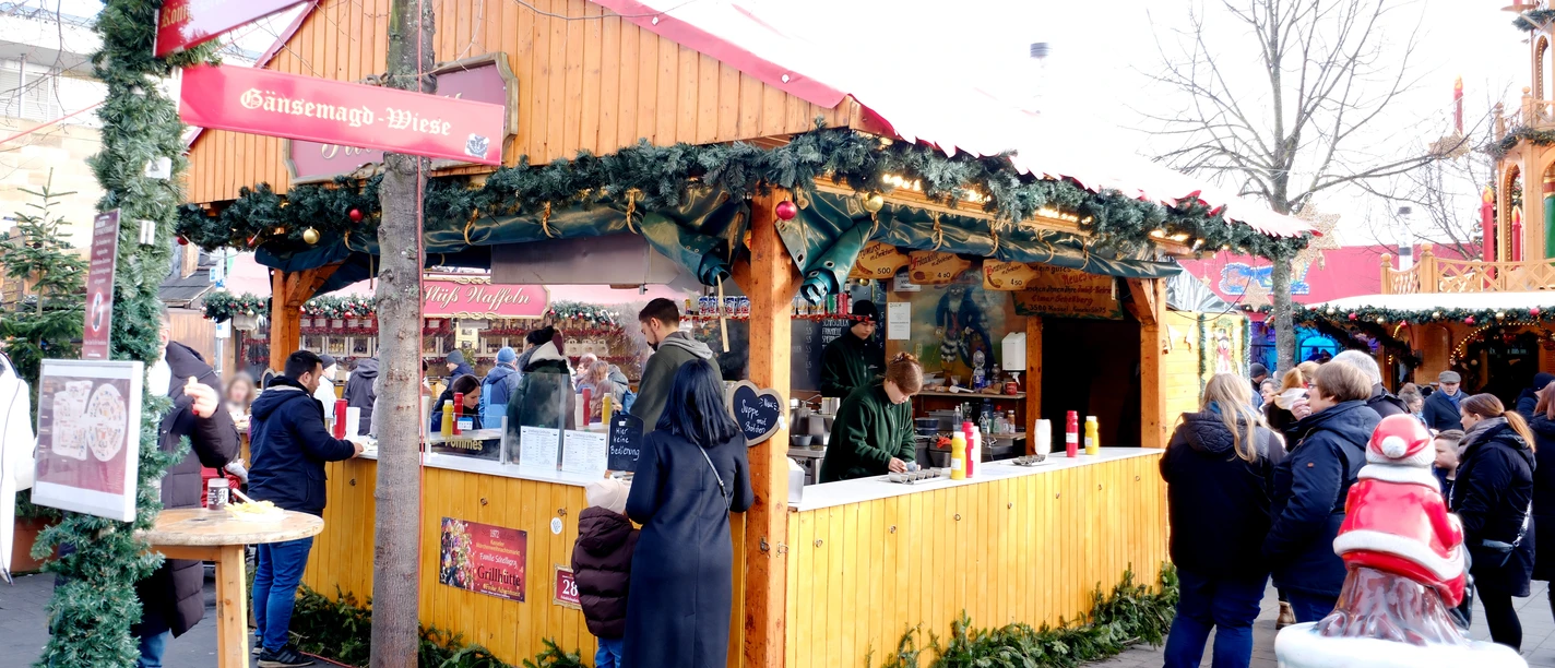 Grill Hütte | Märchenweihnachtsmarkt Kassel Eine geschmückte Holzhütte ist sichtbar. Im inneren der Hütte werden die Speisen zubereitet.