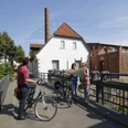 Radwanderer vor dem Tuchmacher Museum in Bramsche Drei Radfahrer studieren eine Karte vor einer historischen Wassermühle an einem sonnigen Tag.