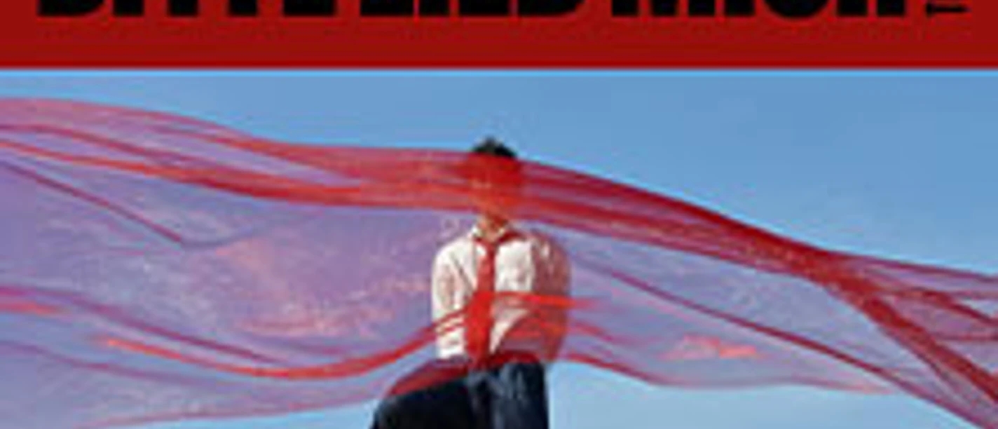 Rotes Tourmotiv „Bitte lieb mich“ mit sitzender Person unter transparentem Tuch vor blauem Himmel