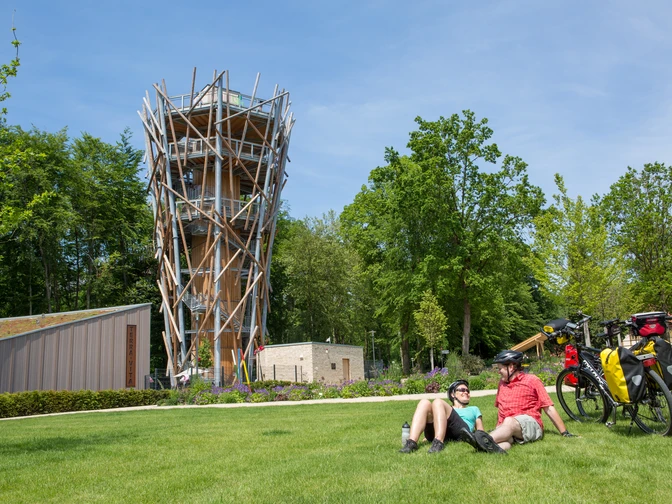 Radlerrast in Bad Iburg Zwei Radfahrer entspannen auf einer Wiese vor einem hölzernen Aussichtsturm bei sonnigem Wetter.