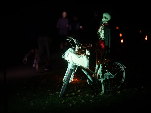 Sparda-Bank Halloween-Run Köln Beleuchtetes Skelett am Fahrrad, dahinter Läufer beim Halloween-Run im Dunkeln