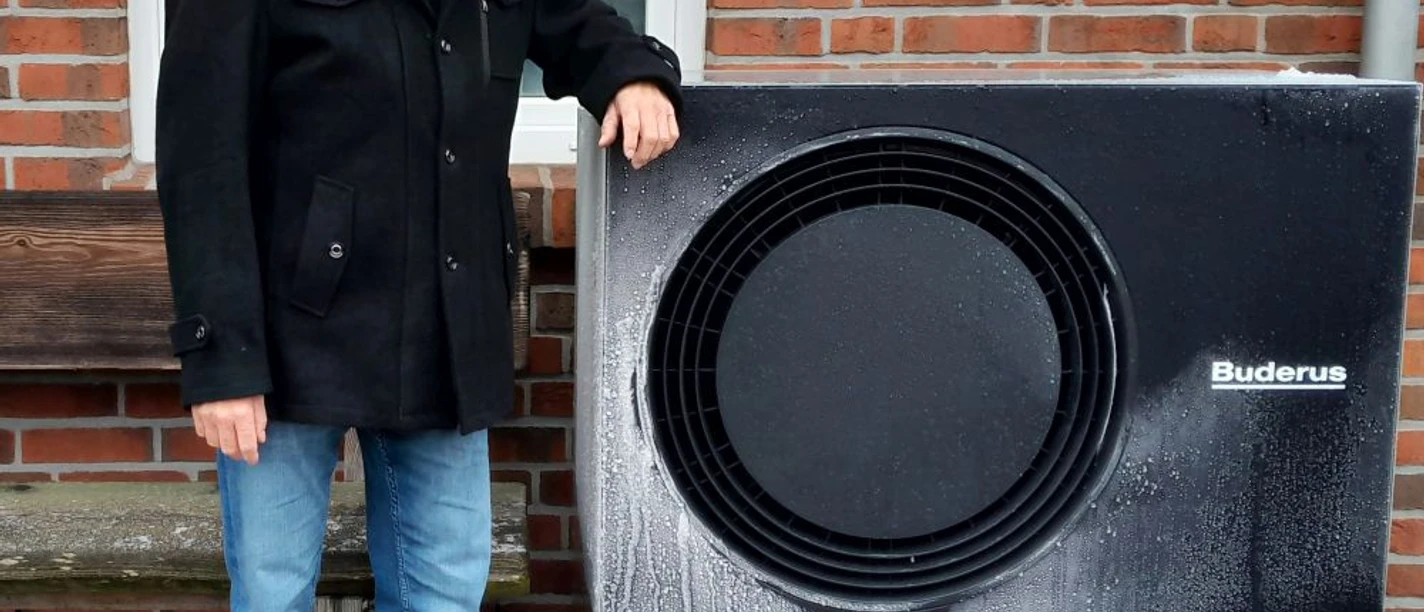 Andreas Stampa neben Wärmepumpe Andreas Stampa steht vor einer Backsteinwand neben einer schwarzen Wärmepumpe.